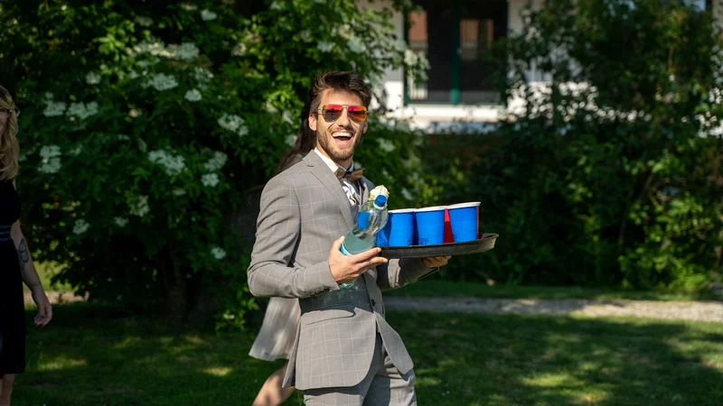 RawmanPictures - Sebastian Schiefermayr | Hochzeit Traude & Gerhard | Mann in Anzug mit Getränken, fröhliche Gartenparty, Eventfotografie, Sommerlichen Moment festhalten.