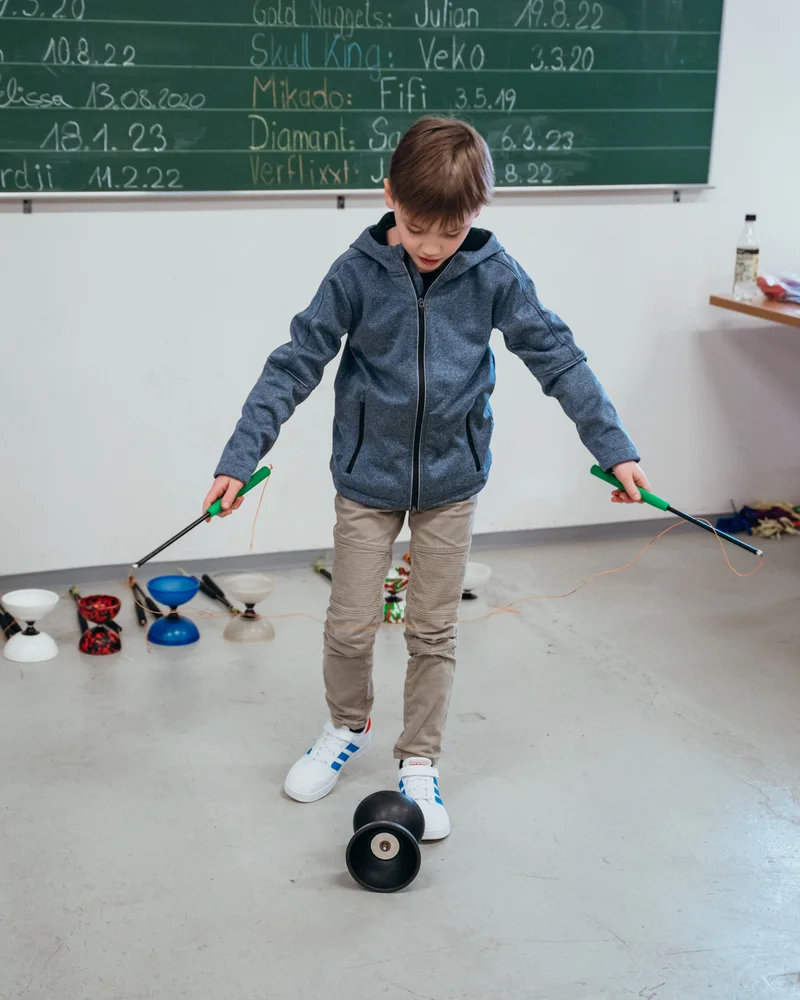 RawmanPictures - Sebastian Schiefermayr | Jonglierworkshop Marchtrenk | Ein Kind übt Diabolo jonglieren in einer Schulumgebung. Freizeitaktivitäten lernen.
