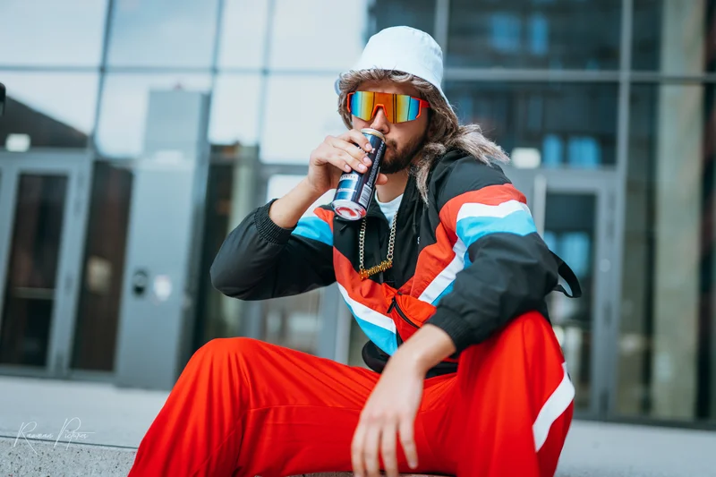 RawmanPictures - Sebastian Schiefermayr | Musikvideodreh "Flinz Asozial" | Trendige Streetwear-Fotografie eines stilvollen jungen Mannes mit Energy-Drink im urbanen Umfeld.