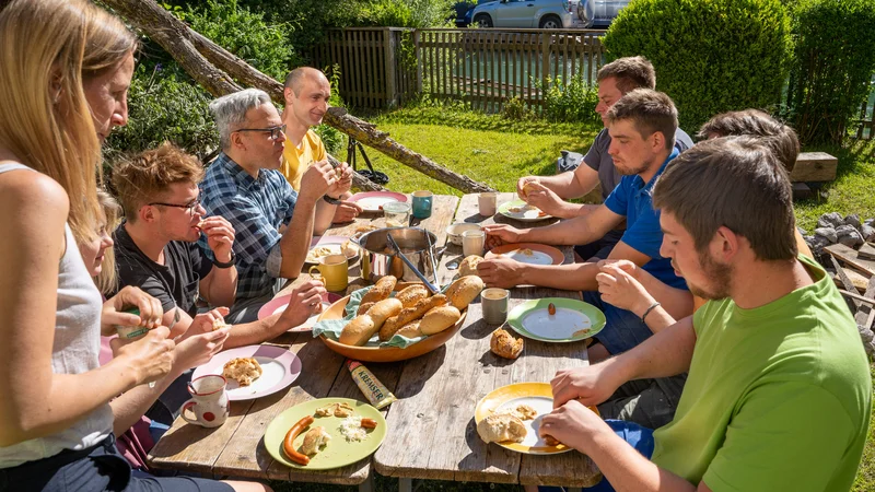 RawmanPictures - Sebastian Schiefermayr | Sägewerk Löberbauer | Outdoor-Familienfrühstück im Garten bei Sonnenschein. Tisch mit Brötchen und Kaffee gedeckt.