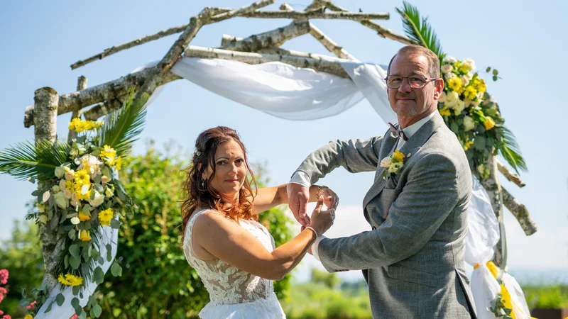 RawmanPictures - Sebastian Schiefermayr | Hochzeit Traude & Gerhard | Hochzeitsfotografie: Brautpaar vor blumengeschmücktem Traubogen im Freien.