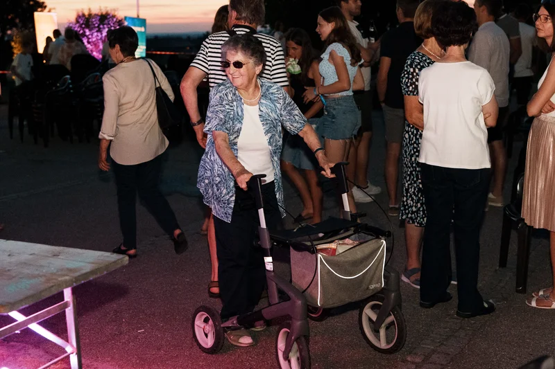 RawmanPictures - Sebastian Schiefermayr | Singkreis-Sundowner  | Ältere Dame mit Rollator auf lebhafter Veranstaltung bei Sonnenuntergang. Eventfotografie.