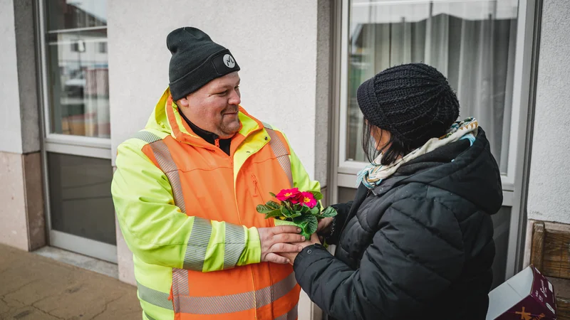 RawmanPictures - Sebastian Schiefermayr | Valentinsaktion Marchtrenk | Person überreicht Blumenstrauß in Winterkleidung, emotionale Begegnung im Freien, Straßenfotografie.