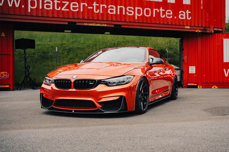 RawmanPictures - Sebastian Schiefermayr | Motortag Salzburg 2025 | Leuchtend orangefarbener Sportwagen vor Containerkulisse – Dynamik und Stil in urbaner Szene.