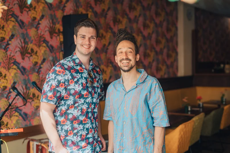 RawmanPictures - Sebastian Schiefermayr | Charity Brunch | Zwei Männer in einem bunt gestalteten Café zeigen Mode und Lebensfreude.