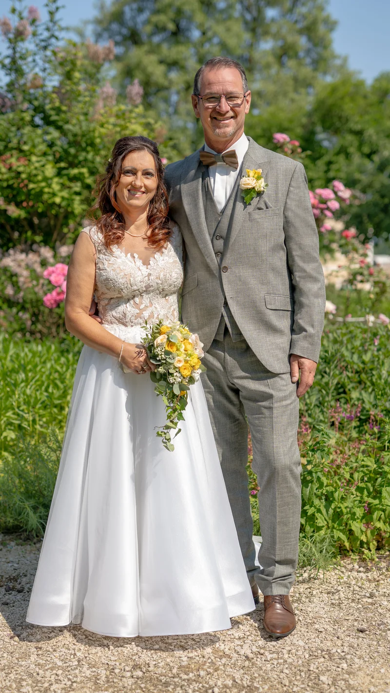 RawmanPictures - Sebastian Schiefermayr | Hochzeit Traude & Gerhard | Elegante Hochzeitsfotografie im Garten mit Brautpaar und blühenden Blumen im Hintergrund.