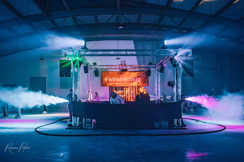 RawmanPictures - Sebastian Schiefermayr | Eisdisco Saisonfinale 2024 | Beleuchtete Bühne mit DJ-Setup, Nebeleffekten und Farblicht in Industriekulisse.