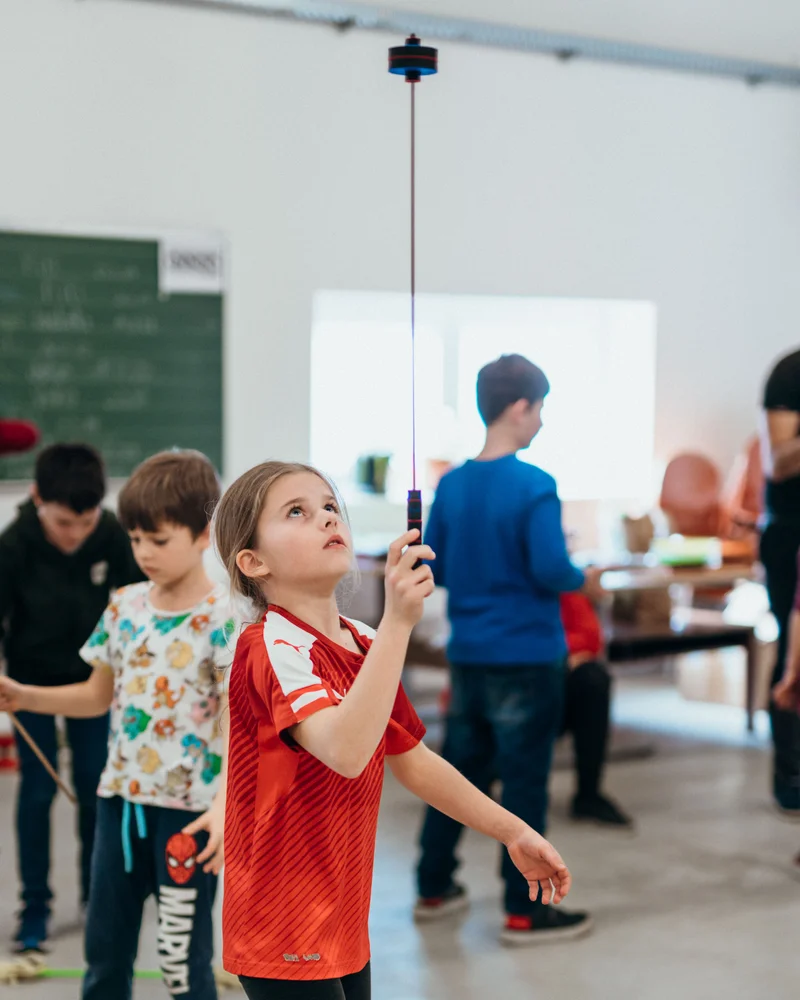 RawmanPictures - Sebastian Schiefermayr | Jonglierworkshop Marchtrenk | Kinder beim Balancieren eines Spielzeugs in einem Gemeinschaftsraum. Kinderfotografie Veranstaltungen.