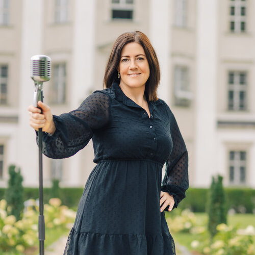 RawmanPictures - Sebastian Schiefermayr | Portraitshooting Tamara R. | Sängerin mit Retro-Mikrofon vor historischer Kulisse, Porträtfotografie im Freien.