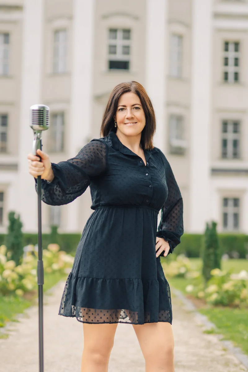 RawmanPictures - Sebastian Schiefermayr | Portraitshooting Tamara R. | Sängerin mit Retro-Mikrofon vor historischer Kulisse, Porträtfotografie im Freien.