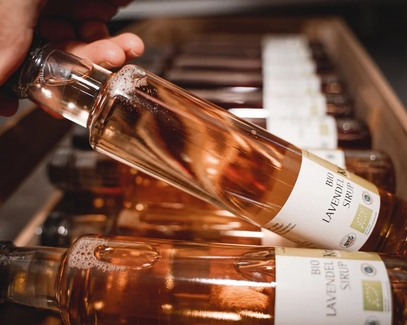 RawmanPictures - Sebastian Schiefermayr | Kräuter­manufaktur Sallmannsberg | Flaschenfotografie: Hochwertiger Lavendelblüten-Sirup im Regal - natürliches Produkt im Fokus.