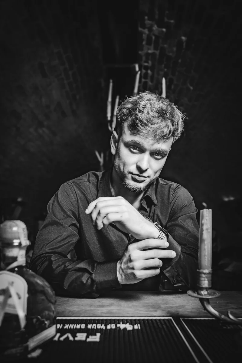 RawmanPictures - Sebastian Schiefermayr | Portraitshooting Kevin F. | Schwarz-Weiß-Porträtfotografie eines Mannes in stimmungsvoller Bar-Atmosphäre.