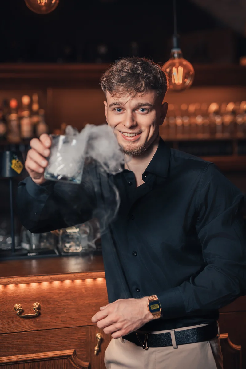 RawmanPictures - Sebastian Schiefermayr | Portraitshooting Kevin F. | Junger Mann an einer stilvollen Bar mit rauchigem Cocktail und edler Atmosphäre.