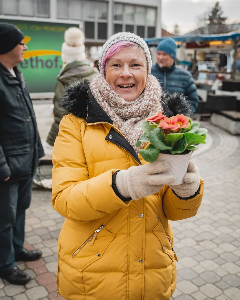 RawmanPictures - Sebastian Schiefermayr | Valentinsaktion Marchtrenk | Fröhliche Wintermarktszene mit Frau und Blume, festgehalten von einem kreativen Fotografen.