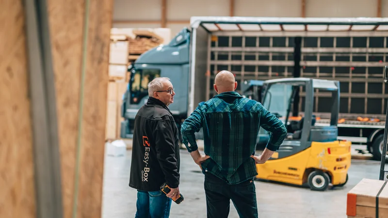 RawmanPictures - Sebastian Schiefermayr | Firmenshooting EasyBox GmbH | Industrielle Lagerlogistik: Mitarbeiter im Gespräch vor Lastwagen und Gabelstapler.
