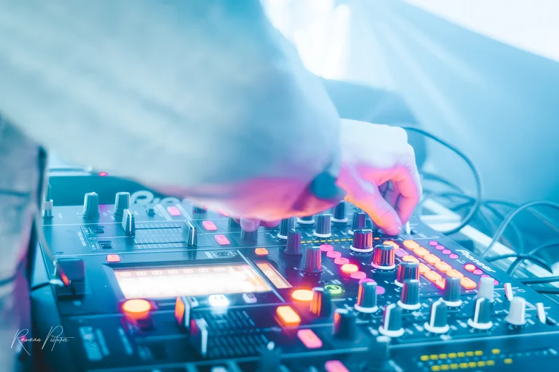 RawmanPictures - Sebastian Schiefermayr | Eisdisco Marchtrenk | DJ mischt Musik auf bunt beleuchtetem Mischpult in dynamischer Veranstaltungsszene.
