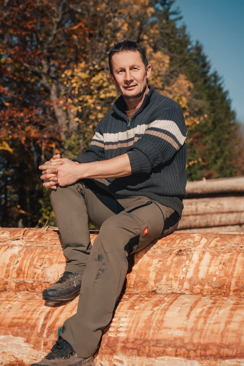 RawmanPictures - Sebastian Schiefermayr | Sägewerk Löberbauer | Outdoor-Portraitfotografie: Mann sitzend auf Holzstamm im herbstlichen Wald.