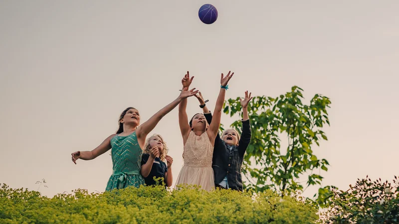 RawmanPictures - Sebastian Schiefermayr | Hochzeit Traude & Gerhard | Kinder spielen draußen mit einem Ball, Naturfotografie, fröhliche Momente, Sommerabend.