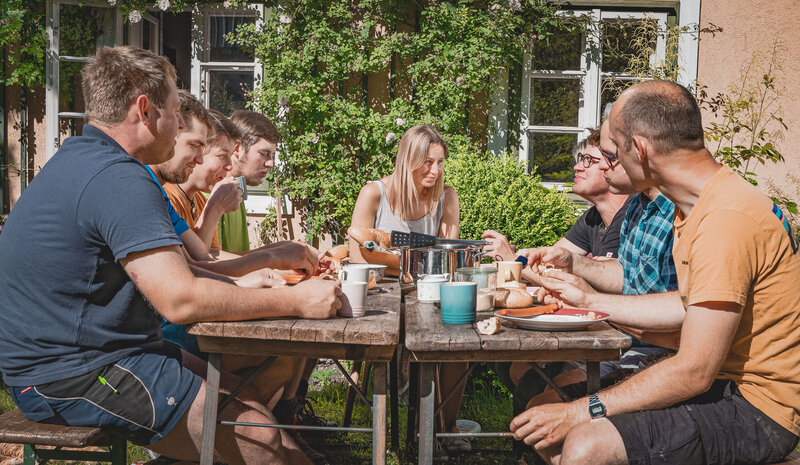 RawmanPictures - Sebastian Schiefermayr | Sägewerk Löberbauer | Fröhliche Outdoor-Gruppe beim gemeinsamen Essen im Sommer, natürliche Fotografie, gesellig.