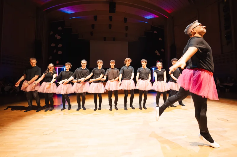 RawmanPictures - Sebastian Schiefermayr | Maturaball HTL1 | Lustiges Ballett-Ensemble auf Bühne in Rosarock mit schwarzen Outfits, beleuchtet. Tanzvorführung.