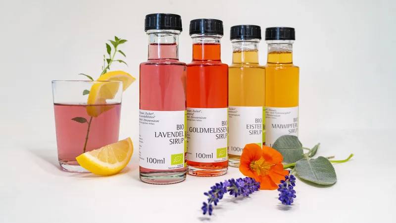 RawmanPictures - Sebastian Schiefermayr | Kräuter­manufaktur Sallmannsberg | Bio-Sirup-Flaschen mit Blüten und Glas, ideal für Getränke und kreative Rezeptfotografie.