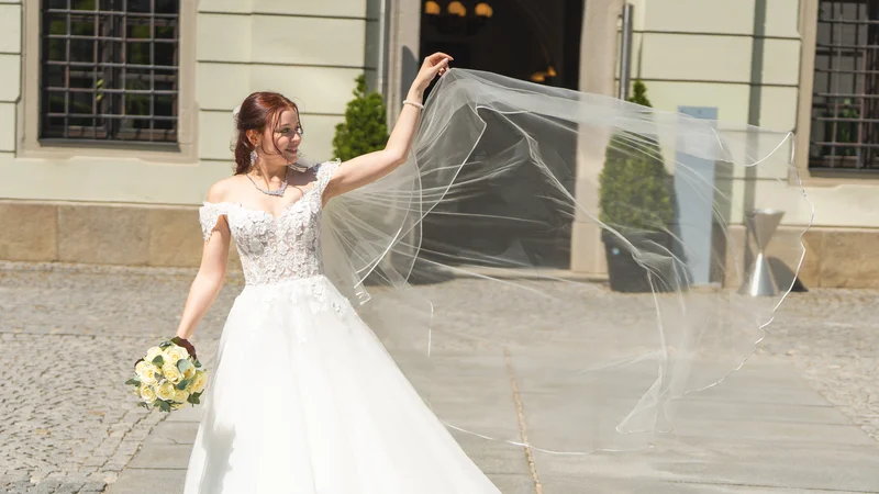 RawmanPictures - Sebastian Schiefermayr | Hochzeit Natalia & Jürgen | Braut mit flatterndem Schleier vor historischem Gebäude, stilvolle Hochzeitsfotografie.