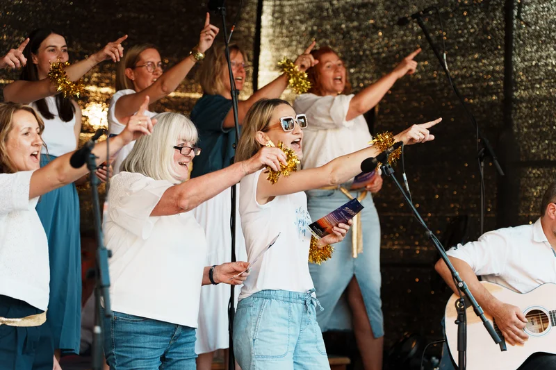 RawmanPictures - Sebastian Schiefermayr | Singkreis-Sundowner  | Chorauftritt mit begeisterten Sängerinnen auf Bühne, lebendige Performance Fotografie.