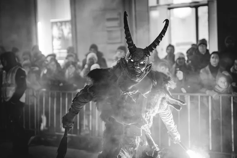 RawmanPictures - Sebastian Schiefermayr | Perchtenlauf Eferding | Schwarz-Weiß-Fotografie eines Maskierten bei Nacht, umgeben von gespannten Zuschauern.