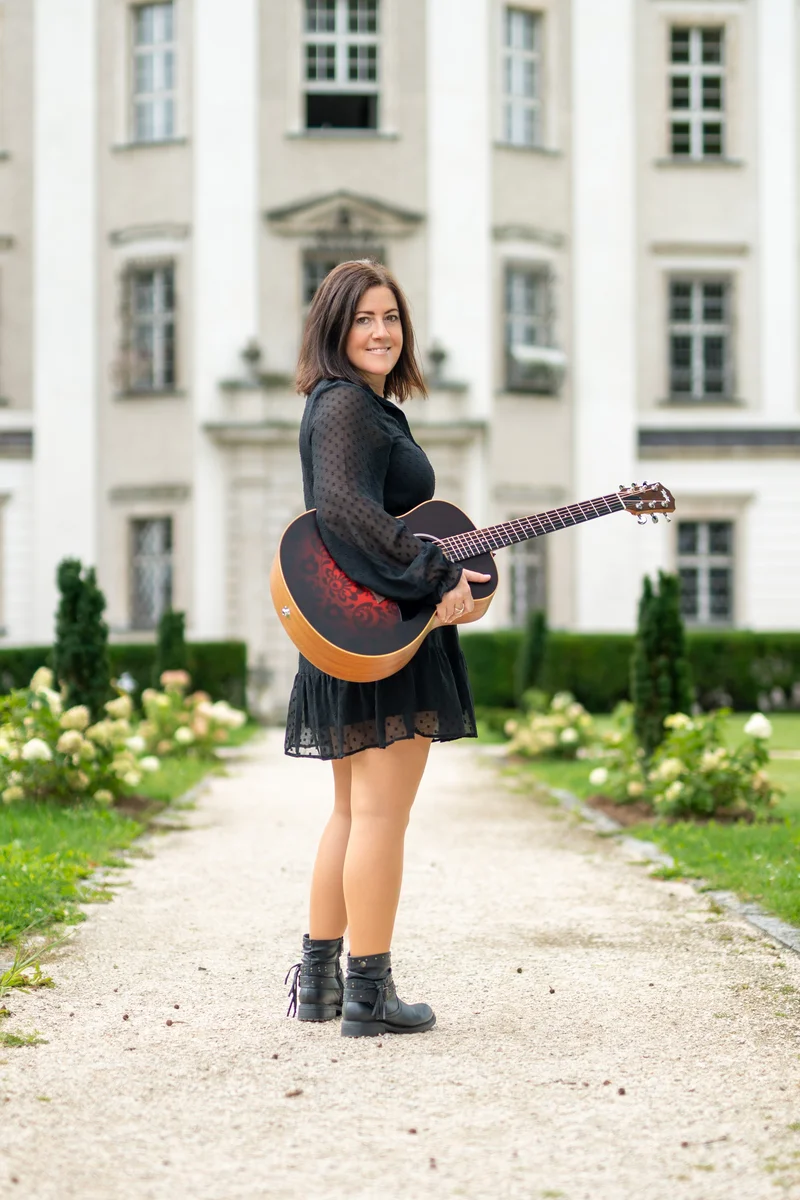 RawmanPictures - Sebastian Schiefermayr | Portraitshooting Tamara R. | Porträtfotografie mit Gitarre vor historischem Gebäude, kreative Outdoor-Fotosession.