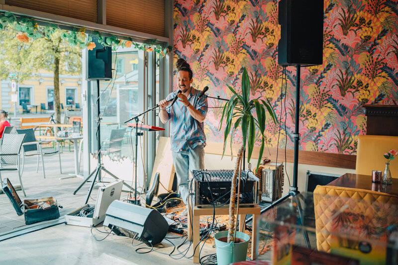 RawmanPictures - Sebastian Schiefermayr | Charity Brunch | Innenraum-Eventfotografie, Musiker spielt live im Café, bunte Wand, entspannte Atmosphäre.