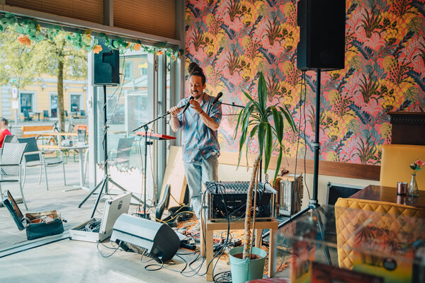 RawmanPictures - Sebastian Schiefermayr | Charity Brunch | Innenraum-Eventfotografie, Musiker spielt live im Café, bunte Wand, entspannte Atmosphäre.