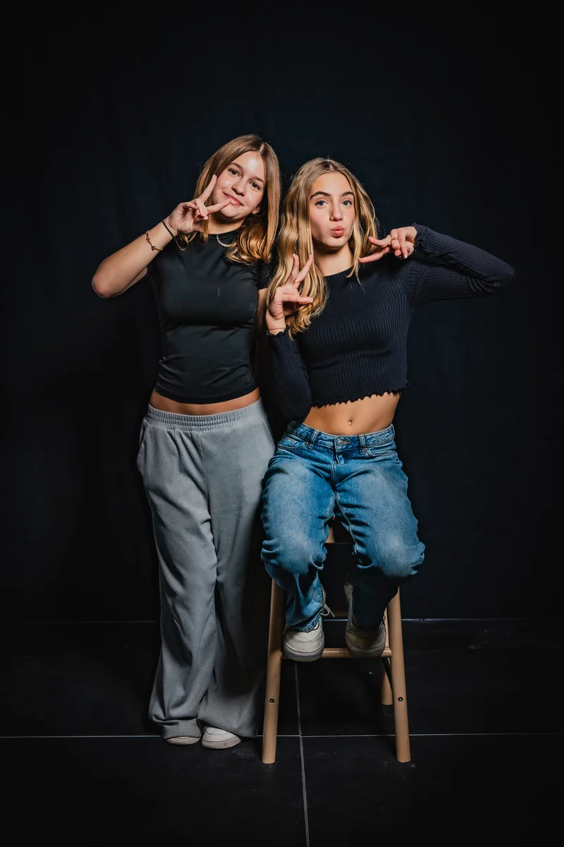 RawmanPictures - Sebastian Schiefermayr | Portrait-Shooting Ozon | Zwei junge Frauen posieren fröhlich vor dunklem Hintergrund im Fotostudio.