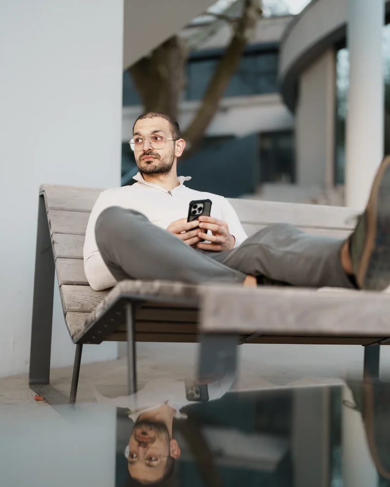 RawmanPictures - Sebastian Schiefermayr | Fotowalk Burhan | Entspannter Mann auf Holzbank mit Smartphone. Zeitgenössische Lifestyle-Fotografie im Freien.