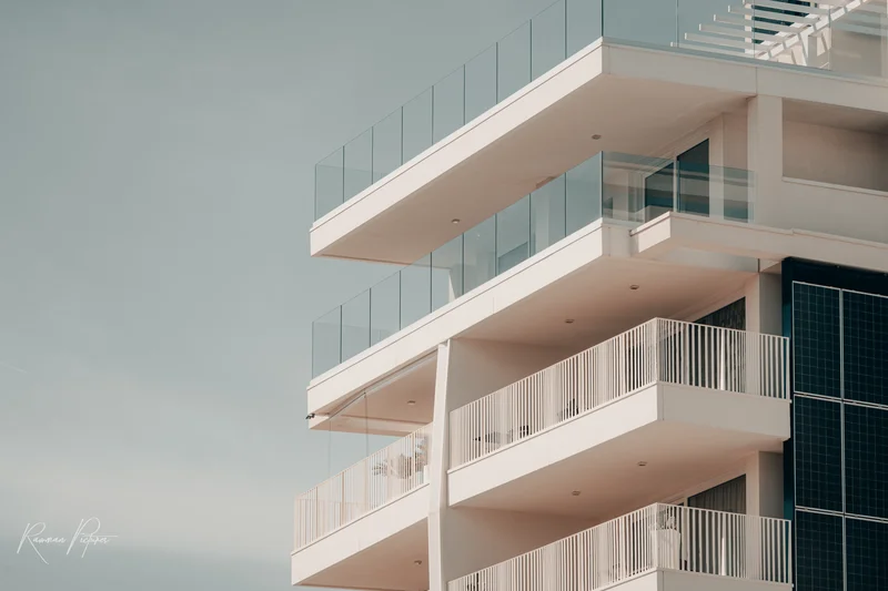 RawmanPictures - Sebastian Schiefermayr | Urlaub Jesolo | Moderne Architektur: Minimalistisches Gebäude mit Glasbalkonen unter klarem Himmel fotografiert.