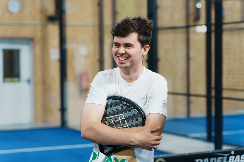 RawmanPictures - Sebastian Schiefermayr | Padelbase Videodreh | Lächelnder Mann auf dem Padelplatz mit Schläger. Sportfotografie, Indoor-Fitness, Padel-Tennis-Spiel.