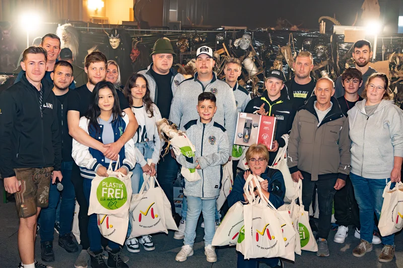 RawmanPictures - Sebastian Schiefermayr | Maskenausstellung | Gruppe von Menschen bei einer Veranstaltung mit nachhaltigen Produkten und Geschenktaschen.