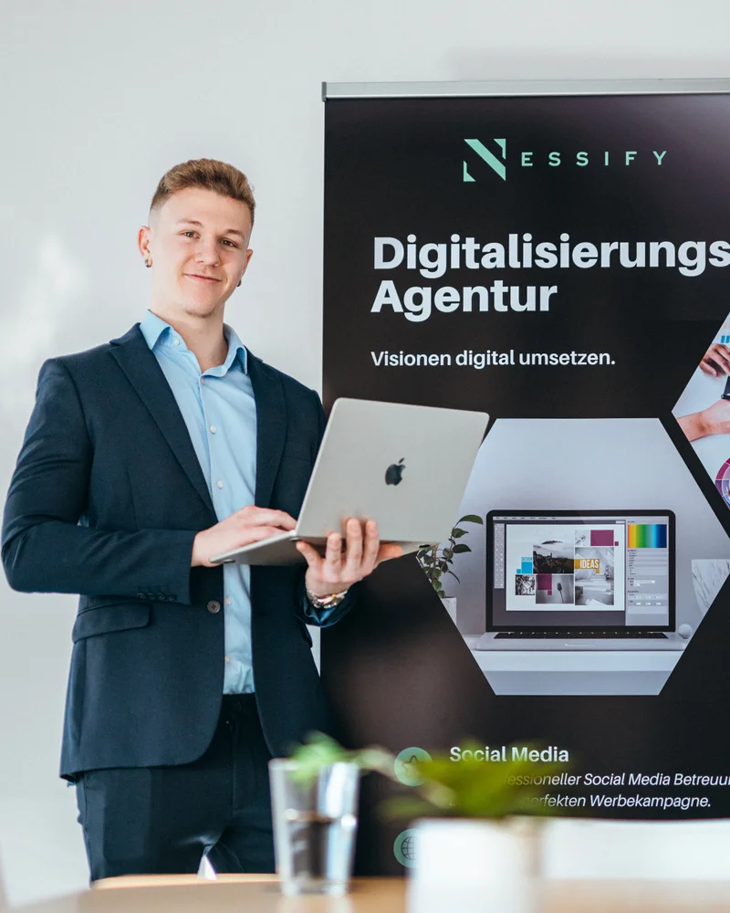 RawmanPictures - Sebastian Schiefermayr | Bussines-Shooting Nessify | Geschäftsmann mit Laptop vor Banner: Digitalisierung, Agentur, Zukunftslösungen.