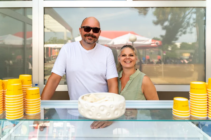 RawmanPictures - Sebastian Schiefermayr | Sommereisdisco | Eisstand im Freien mit freundlichen Verkäufern und gelben Bechern. Sommerliche Straßenfotografie.