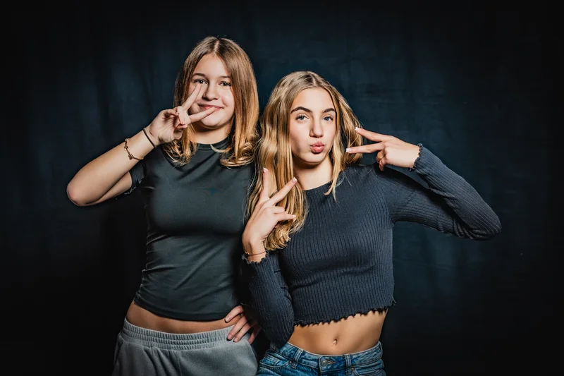 RawmanPictures - Sebastian Schiefermayr | Portrait-Shooting Ozon | Zusammenfassung: Zwei junge Frauen posieren fröhlich vor einem dunklen Hintergrund im Studio.
