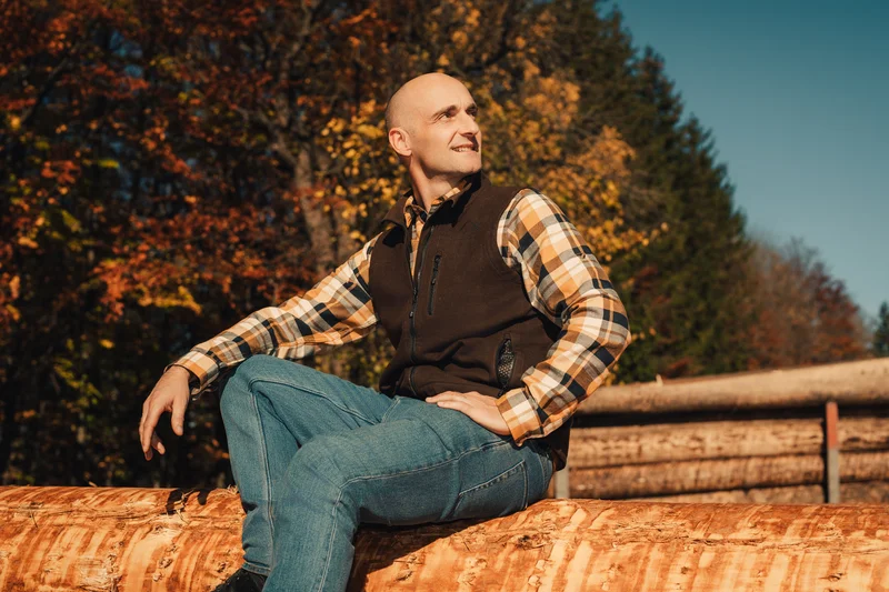 RawmanPictures - Sebastian Schiefermayr | Sägewerk Löberbauer | Outdoor-Porträtfotografie im Herbstlicht, Mann auf Baumstamm, natürliche Farben, rustikaler Stil.