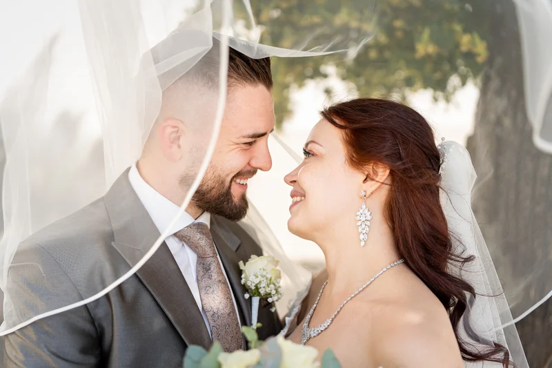 RawmanPictures - Sebastian Schiefermayr | Hochzeit Natalia & Jürgen | Romantische Hochzeitsfotografie im Freien, Brautpaar lächelnd unter dem Schleier.