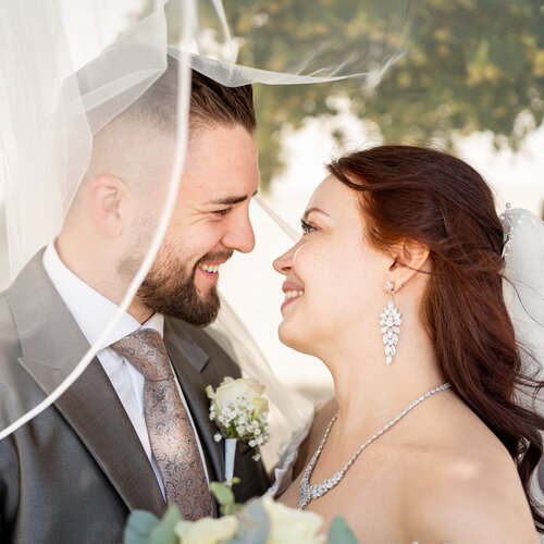 RawmanPictures - Sebastian Schiefermayr | Hochzeit Natalia & Jürgen | Romantische Hochzeitsfotografie im Freien, Brautpaar lächelnd unter dem Schleier.