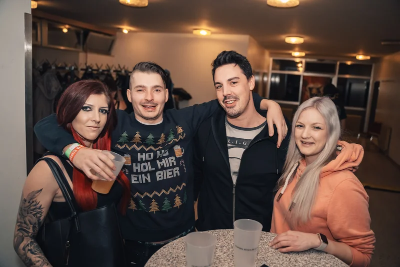 RawmanPictures - Sebastian Schiefermayr | Krampusnacht | Gruppe von Freunden feiert in gemütlicher Barumgebung, lächelnd und mit Getränken in der Hand.