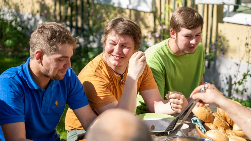 RawmanPictures - Sebastian Schiefermayr | Sägewerk Löberbauer | Gruppe junger Männer bei geselligem Frühstück im Garten. Outdoor-Fotografie, sonniger Morgen.