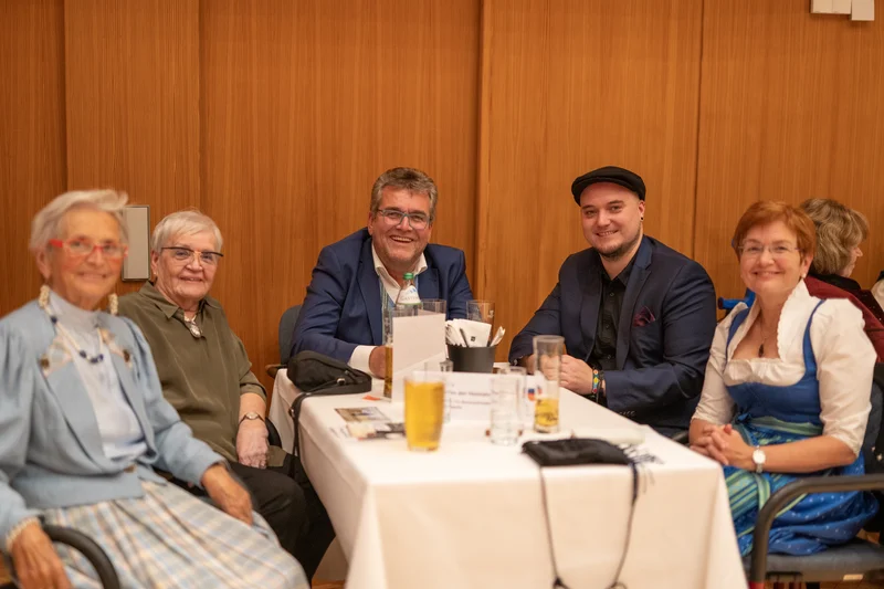 RawmanPictures - Sebastian Schiefermayr | Volkstanzfest | Gruppe von Menschen am Tisch bei einer Feier, festliche Kleidung, geselliges Beisammensein.