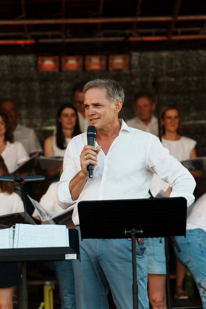 RawmanPictures - Sebastian Schiefermayr | Singkreis-Sundowner  | Mann spricht bei Veranstaltung, Mikro und Notenständer, Abendstimmung, Eventfotografie.