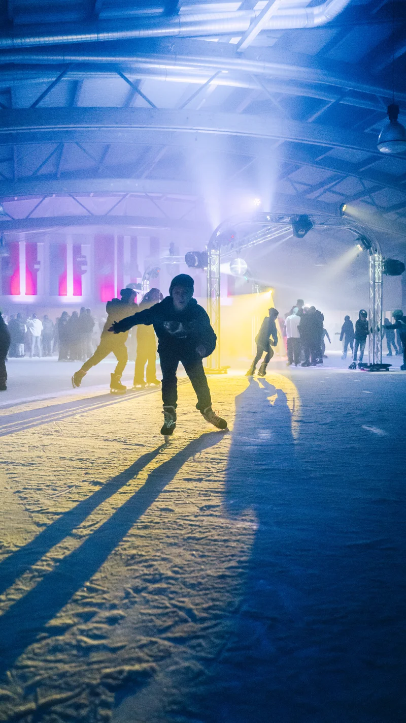 RawmanPictures - Sebastian Schiefermayr | Eisdisco Marchtrenk | Personen beim Eislaufen in farbig beleuchteter Halle, dynamische Bewegung, Freizeitaktivität.