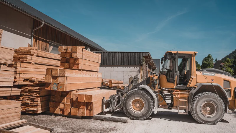 RawmanPictures - Sebastian Schiefermayr | Sägewerk Löberbauer | Bauindustrie Fotografie: Bagger bewegt Holz vor Sägewerk. Baustellen Dokumentation.