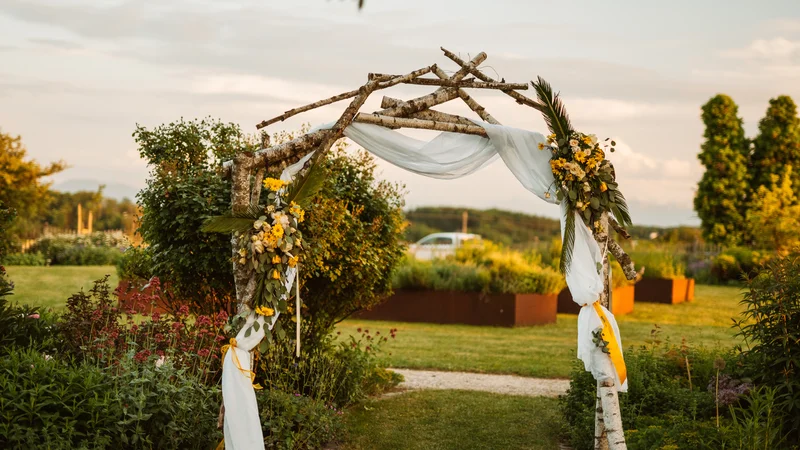 RawmanPictures - Sebastian Schiefermayr | Hochzeit Traude & Gerhard | Romantische Gartenhochzeit: Rustikaler Traubogen mit Blumenarrangement in idyllischer Landschaft.