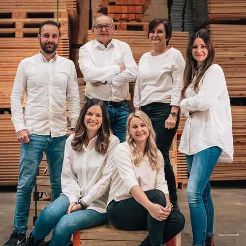 RawmanPictures - Sebastian Schiefermayr | Firmenshooting EasyBox GmbH | Gruppenfoto in Holzwerkstatt: Team im weißen Outfit vor gestapeltem Holz für Firmenwebsite.